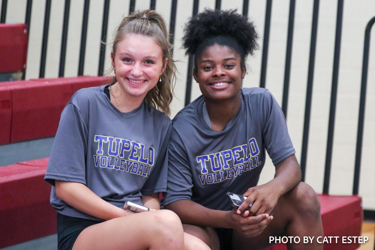 Ella Kinney and Jakala Foulks smile on the bleachers as they cheer their team on.