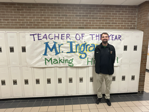 Ingram standing by his teacher of the year banner