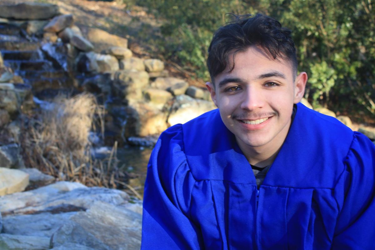 Andrick Flores-Doubleday wearing a graduation gown smiling with scenery behind him 